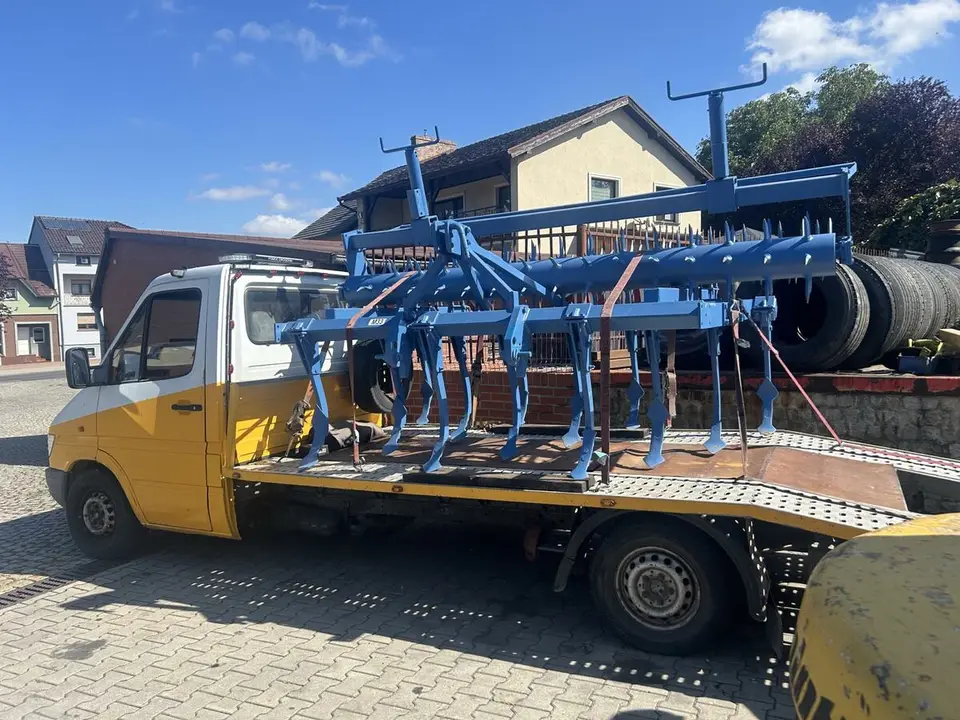 Niebieska maszyna rolnicza przypięta pasami na platformie lawety.